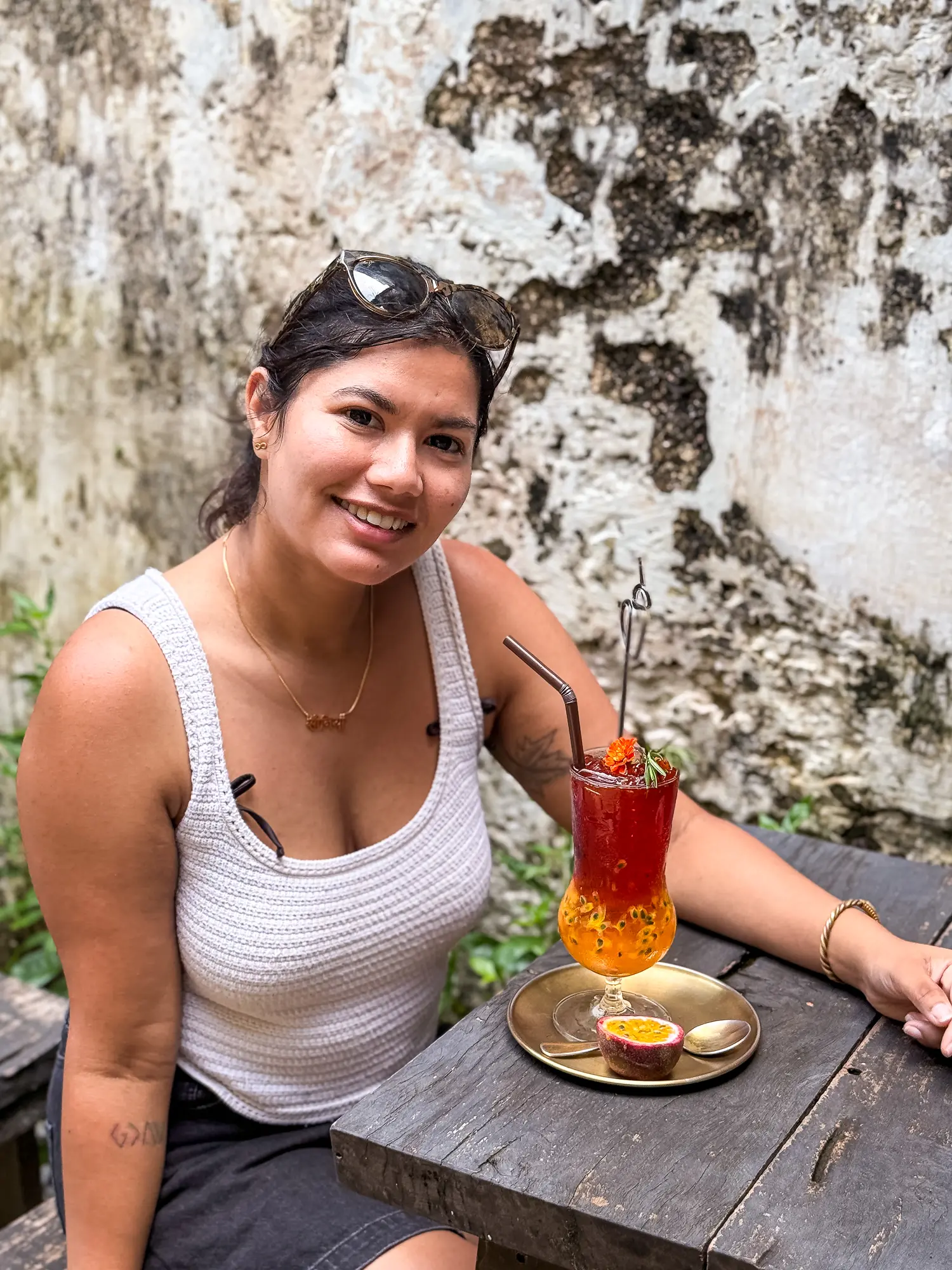 Sonia smiling at an outdoor café beside a passionfruit drink, with a textured wall behind. Promoting the feeling of success from using one of her travel guides.