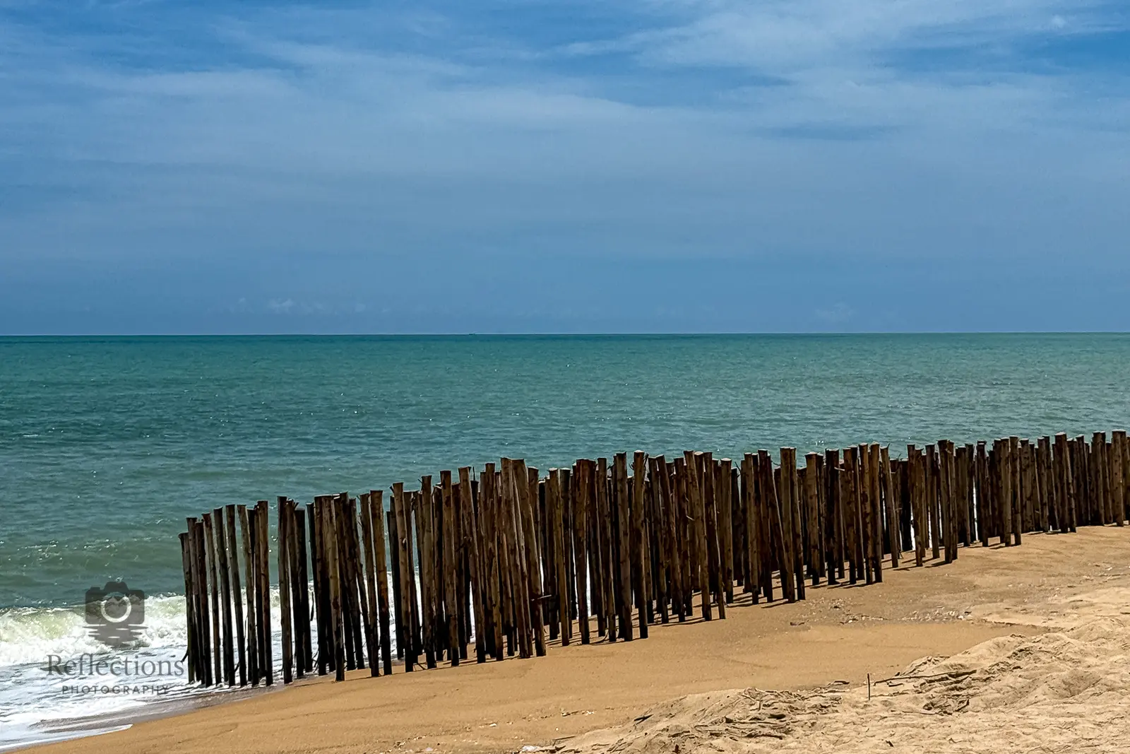 Wooden erosion-control posts on Sai Kaew Beach, Phang Nga, Thailand, with calm Andaman Sea and soft morning sky.