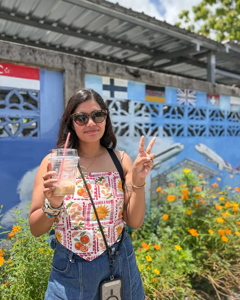 Guest holding iced coffee at Runway Café Phuket with airplane mural and flags