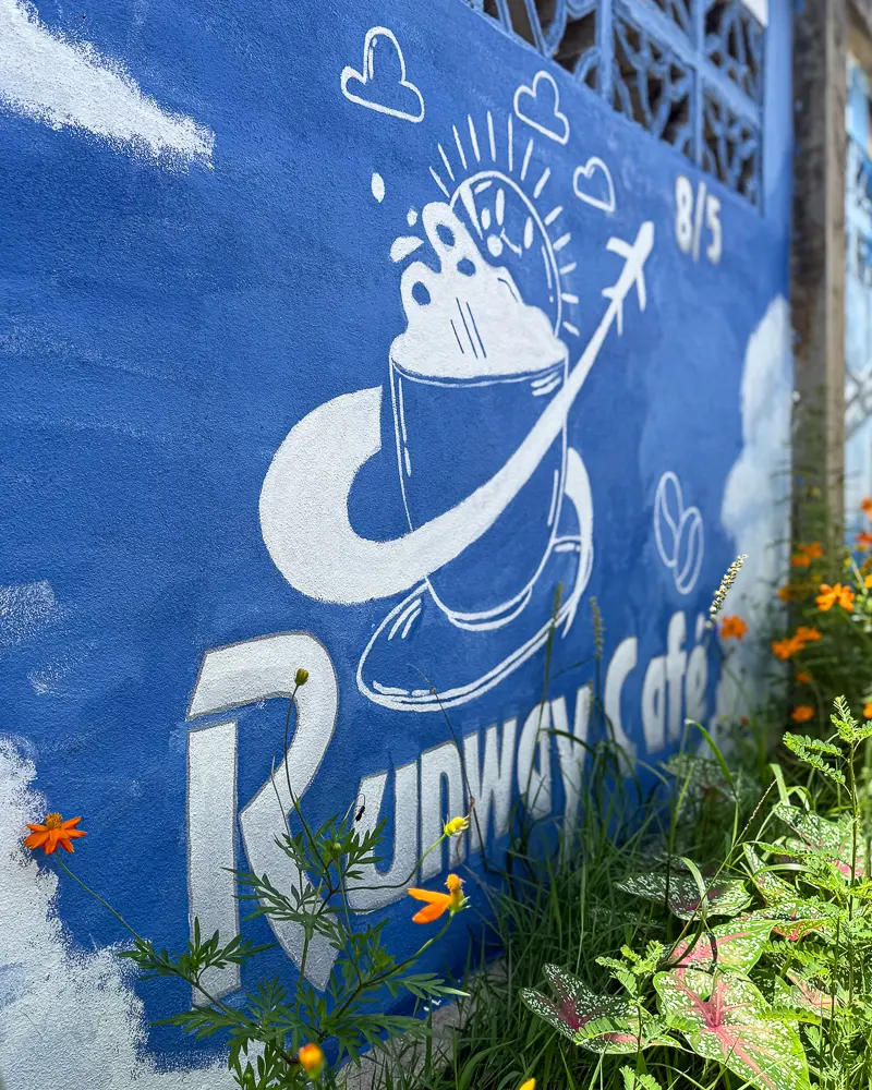 Runway Café Phuket wall logo with orange flowers in the foreground